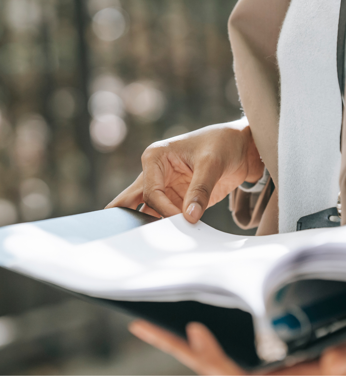 Close up image of hands turning pages of a binder containing documents.